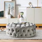 Gray tufted ottoman in a living room setting with decor elements.