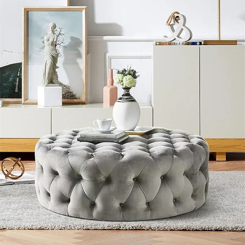 Gray tufted ottoman in a living room setting with decor elements.